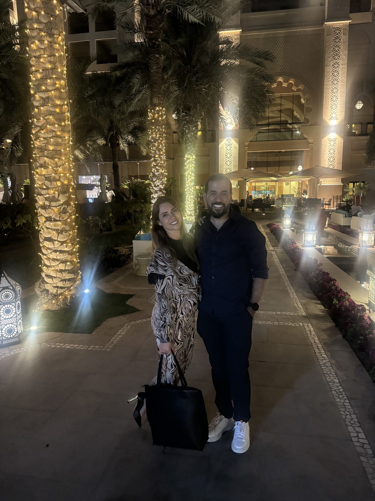 Casal caminhando à noite por um jardim de palmeiras iluminadas em um resort no Oriente Médio