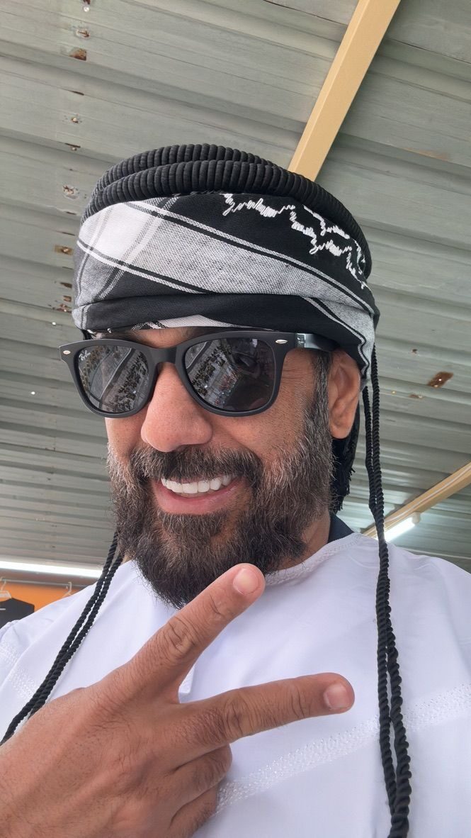 Joaquim sorrindo usando um lenço tradicional árabe (kufiya) e fazendo sinal de paz
